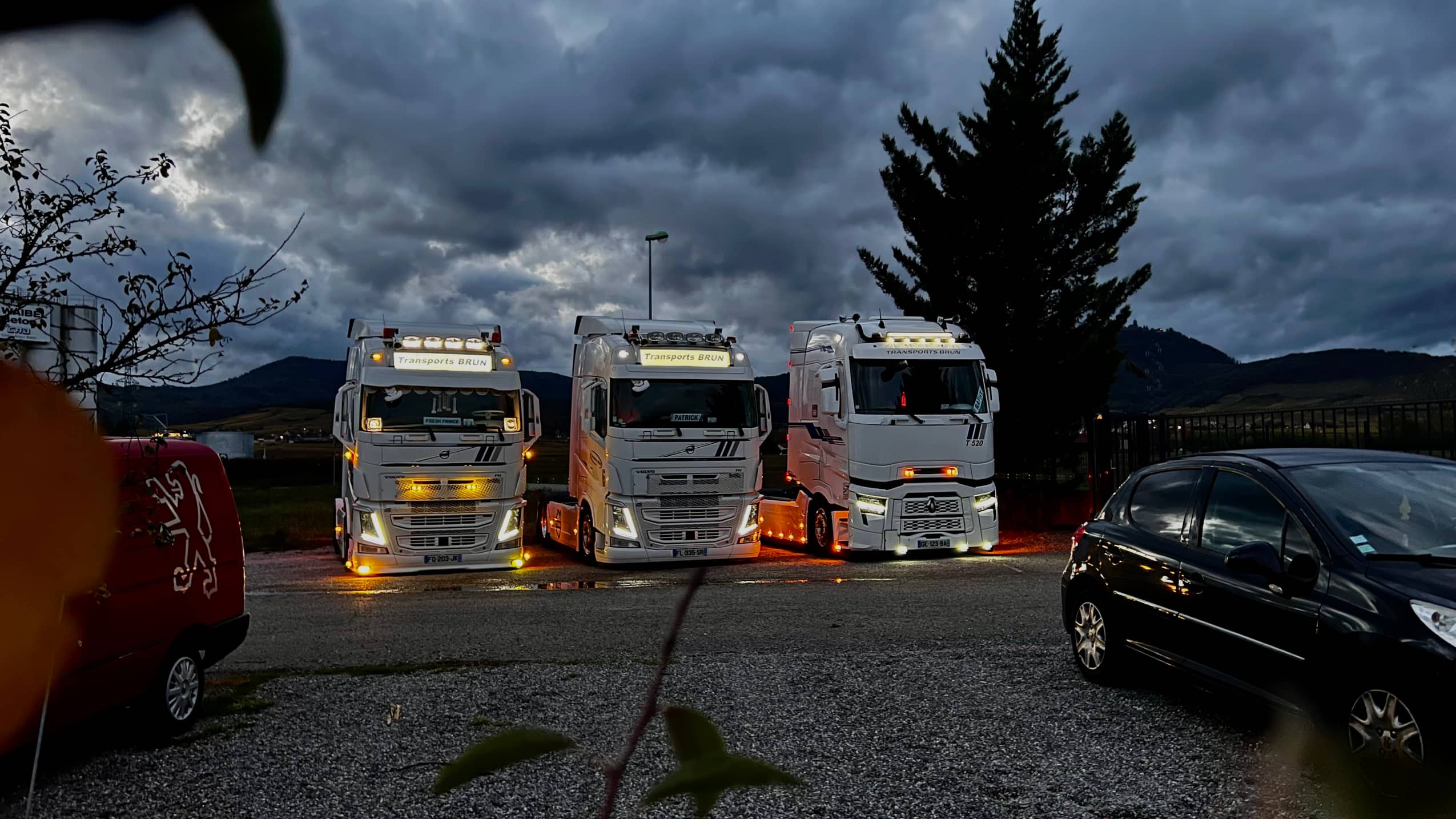 Trois tracteurs de Transports Brun, feux allumés, à la tombée de la nuit