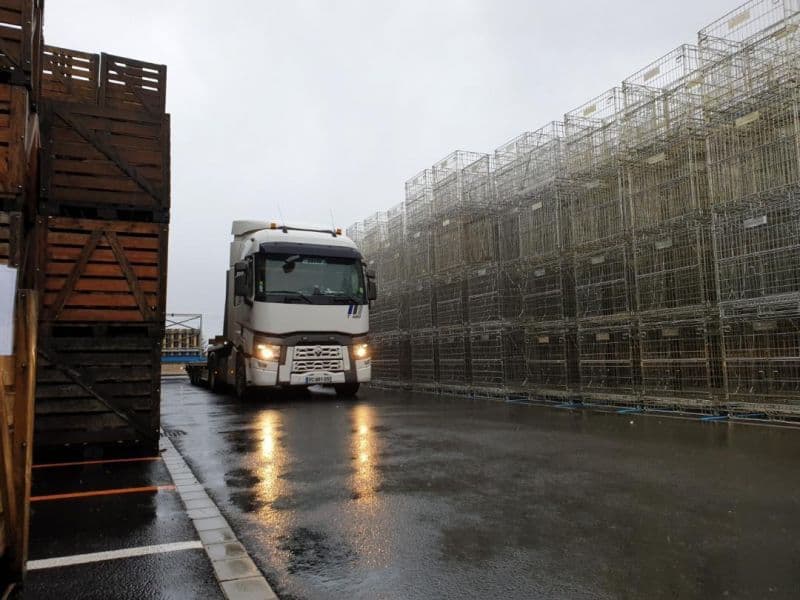 Camion Renault feux allumés entre des piles de caisses-palettes en bois et en grillage