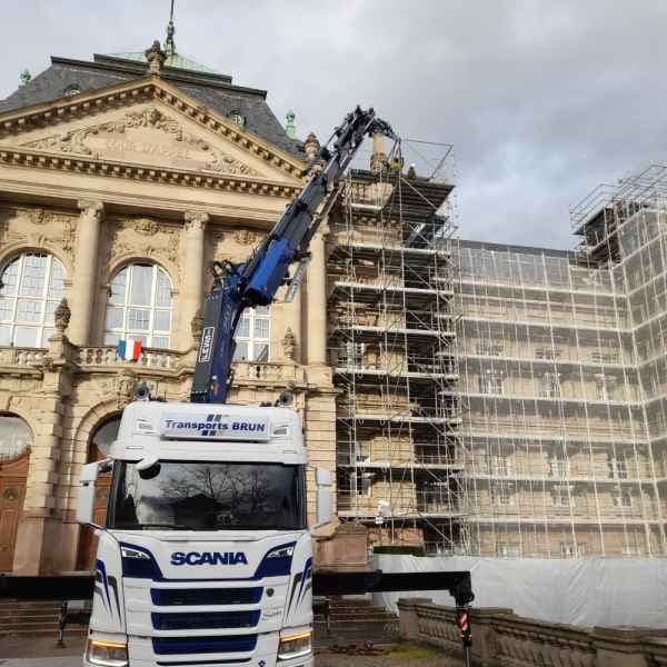 Camion-grue Scania intervenant devant un bâtiment historique en rénovation, sous échafaudage