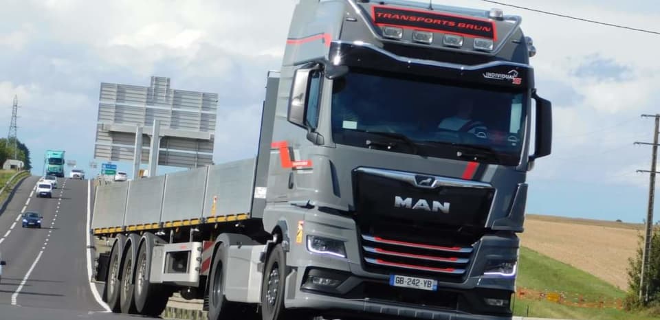 Tracteur MAN gris et semi-remorque plateau sur une voie rapide