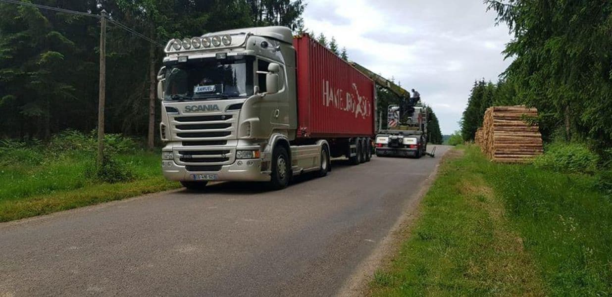 Tracteur Scania tirant un conteneur maritime rouge sur une route forestière